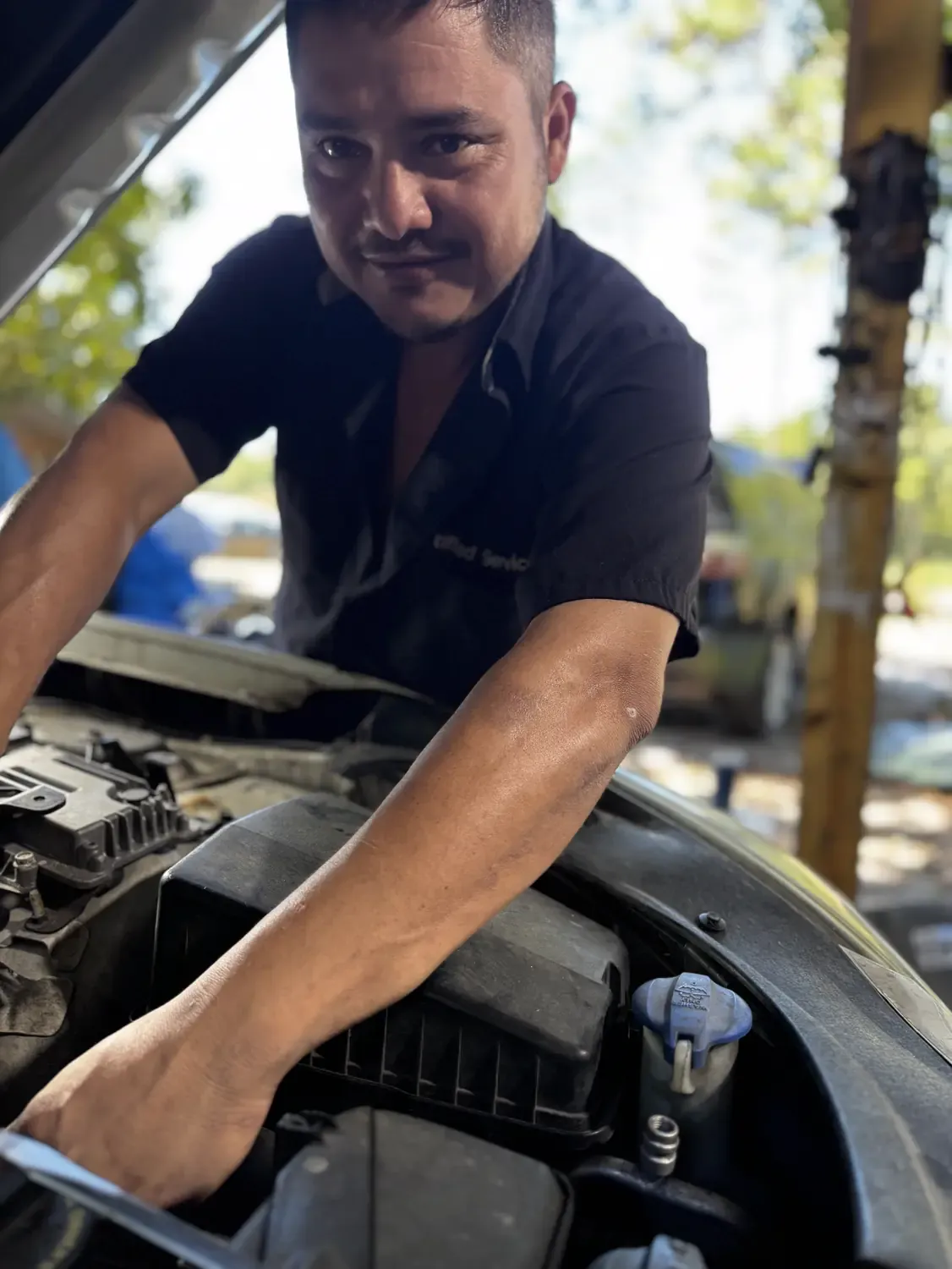 Technician smiling beside a vehicle with the hood raised